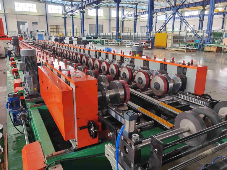 Close-up of the roll former feeder at the entry of the main roll forming section. This unit precisely guides the pre-processed metal sheet into the initial forming rollers, ensuring accurate profile creation.