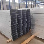 A stack of precisely formed finished cable trays, displaying the characteristic side rails, ventilation slots, and smooth edges, ready for installation in industrial or commercial settings.