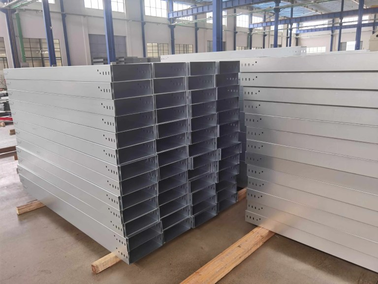 A stack of precisely formed finished cable trays, displaying the characteristic side rails, ventilation slots, and smooth edges, ready for installation in industrial or commercial settings.