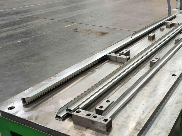 A product inspection station or quality control point, showing an operator or automated sensor checking the dimensions, finish, and integrity of the newly formed solar panel mounting frame components.