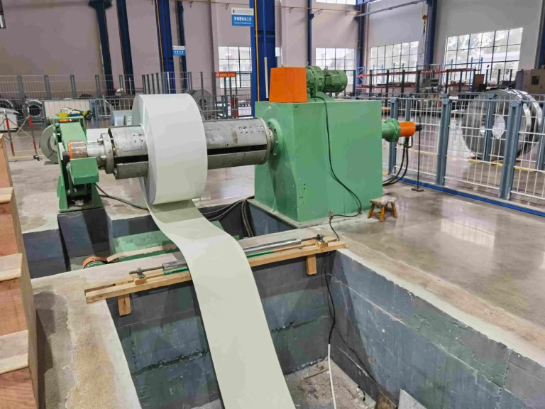 A robust automatic uncoiler for a cable tray roll forming machine, shown holding a large coil of flat sheet metal. The uncoiler precisely feeds the material into the production line, ensuring a smooth and consistent supply without manual intervention.