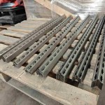 Stapel von präzisionsgeschnittenen, fertig bearbeiteten Metallregalpfosten, die das einheitliche Profil und die durchgehenden Stanzlöcher zeigen.