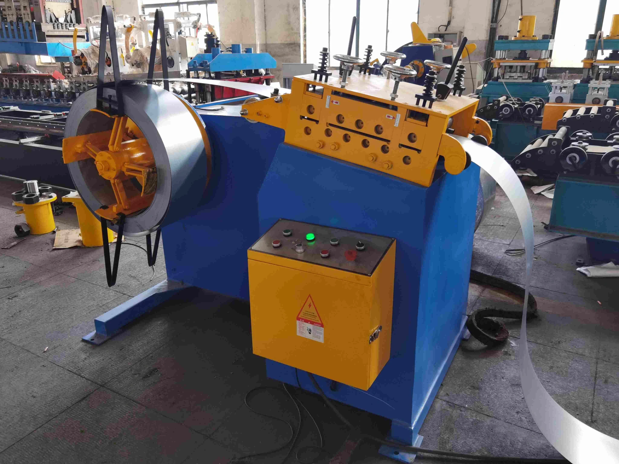 Uncoiler and Leveler machine unwinding and flattening a large steel coil for a door frame roll forming machine.