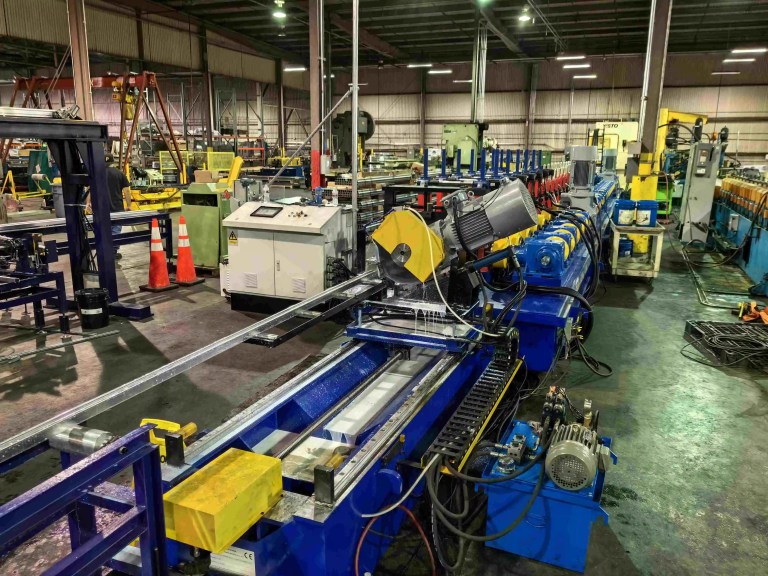ภาพระยะใกล้ของกลไก Servo Flying Shear ที่กำลังประกบกับโปรไฟล์โลหะบนสายการผลิตรีดขึ้นรูป